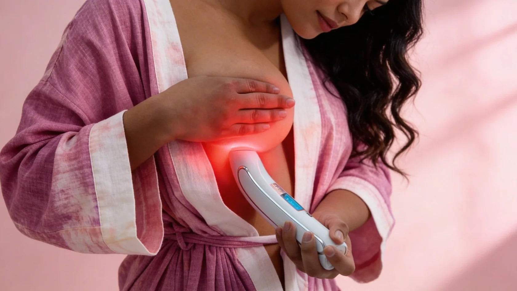 A woman holds the Luminous device flat against her breast in a dim room; the breast glows red from the light passing through it.